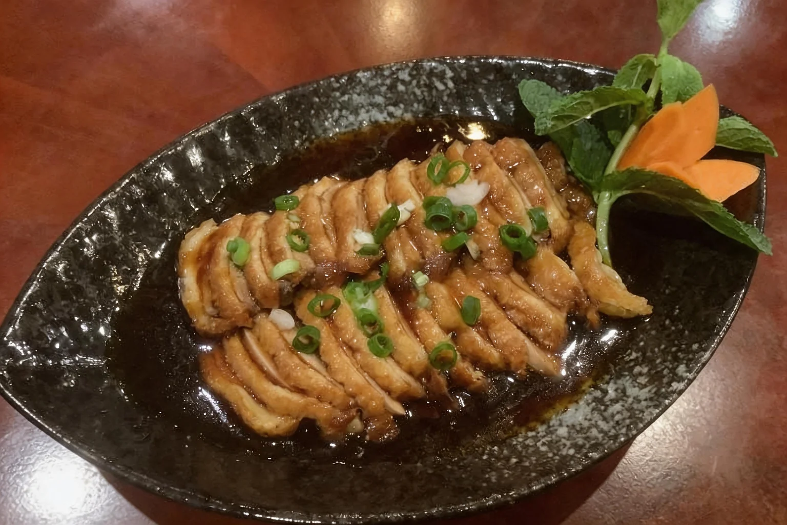 Canard laqué on a black oval dish on a wooden table