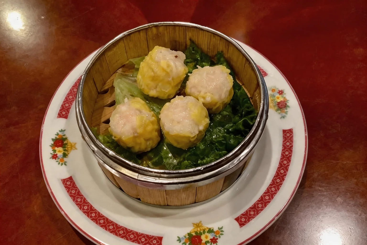 Bouchées de porc "Sio Mai" in a bamboo basket on a plate with a floral pattern