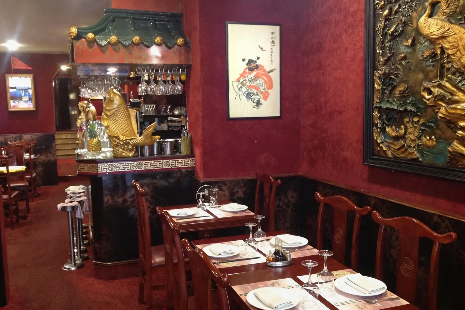Dining room: bar, laid tables and gilded panel on a red wall